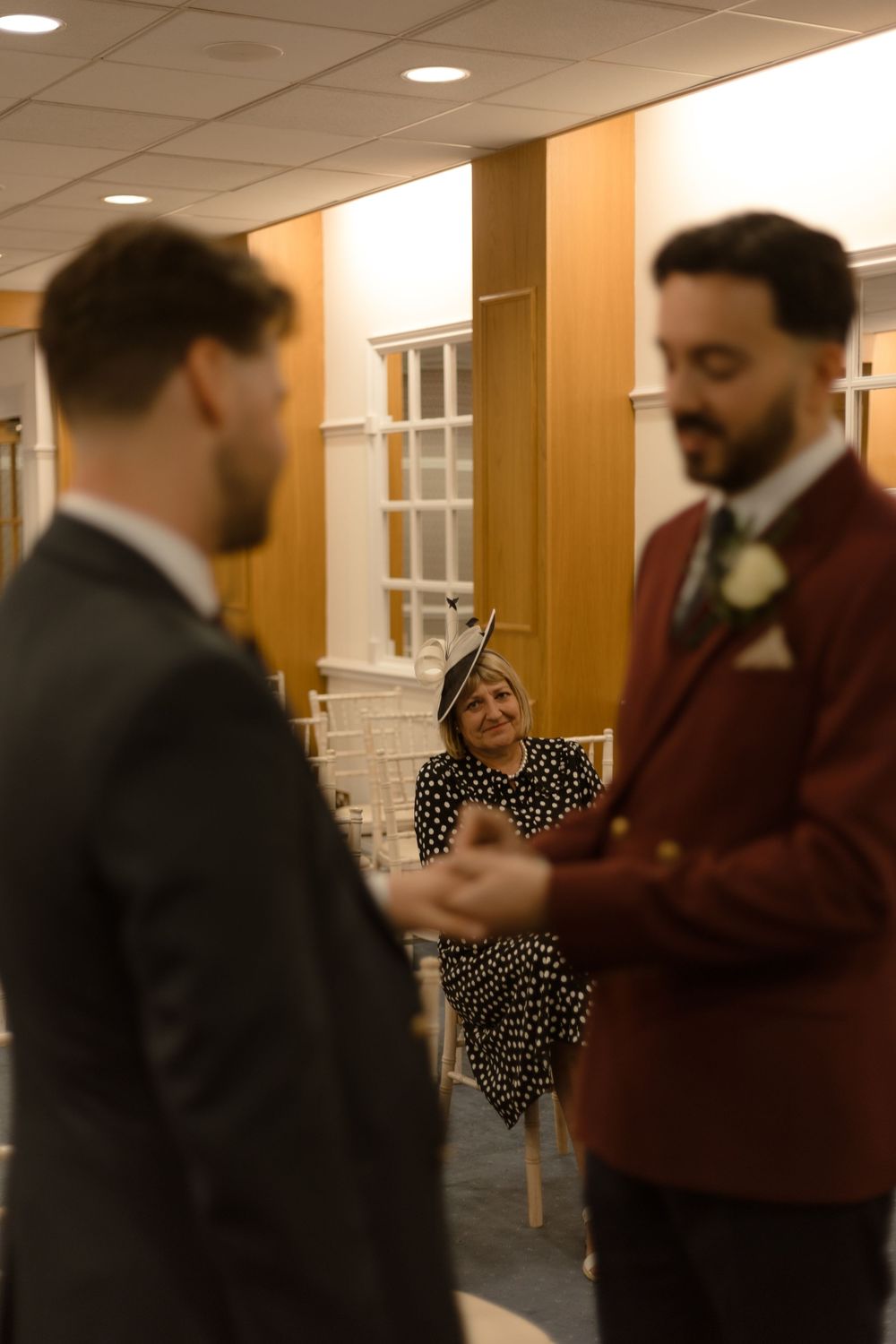 Two people in formal attire converse at a wedding event while a guest in polka dots looks on.