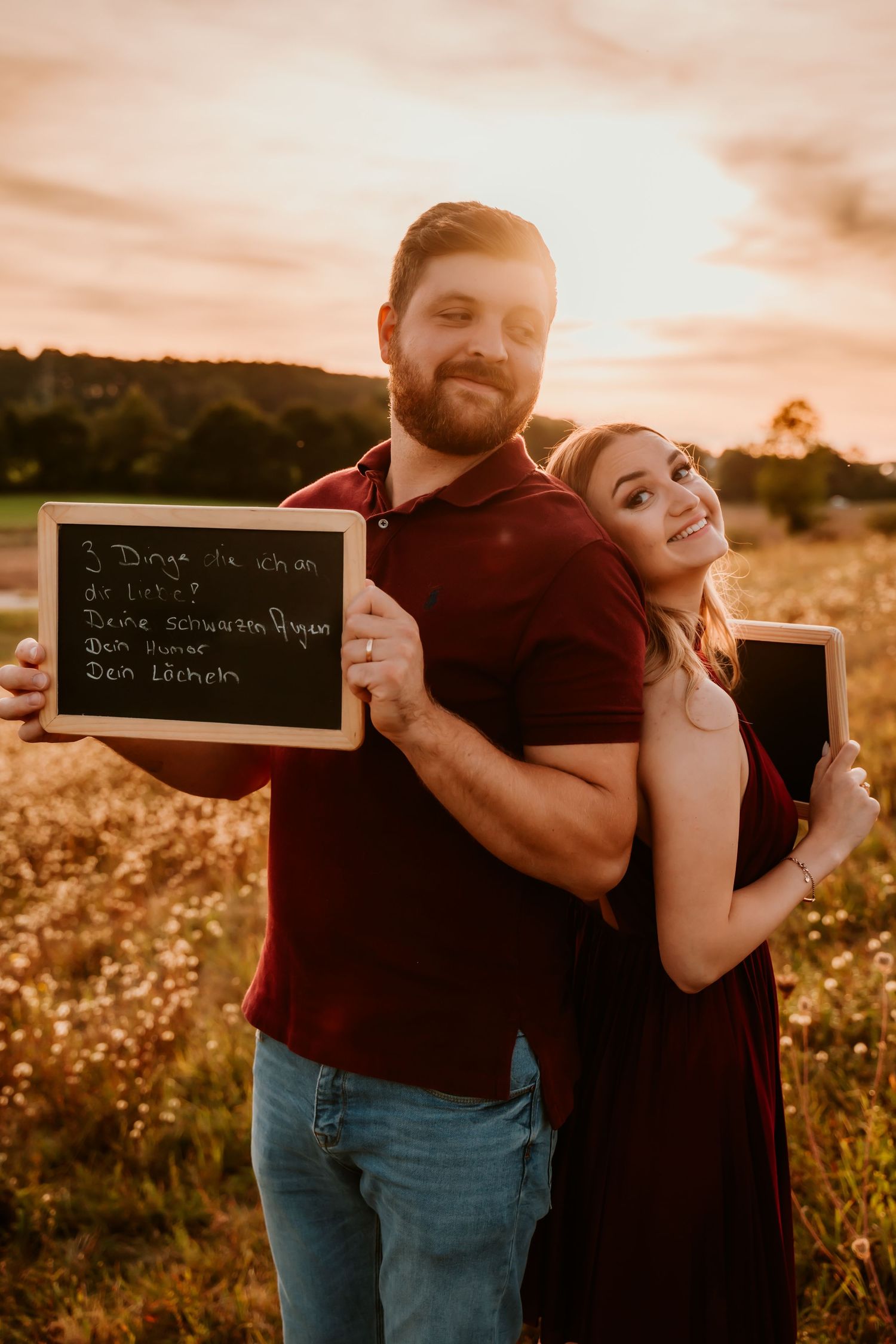 A couple poses back-to-back with chalkboards in a wildflower field at golden hour.
