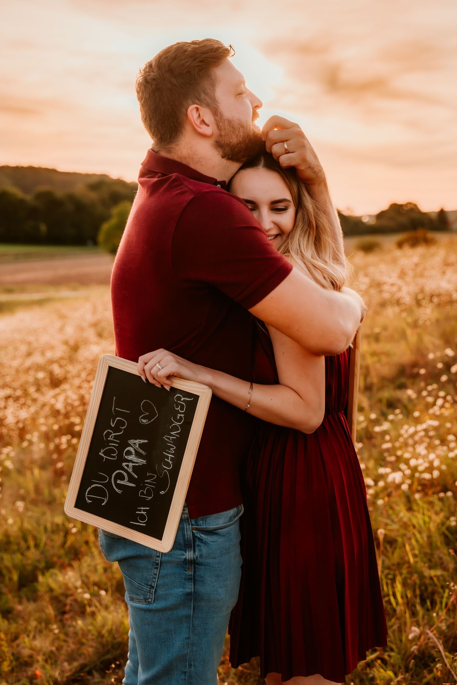 A tender moment captured between two people holding a chalkboard in a golden field.