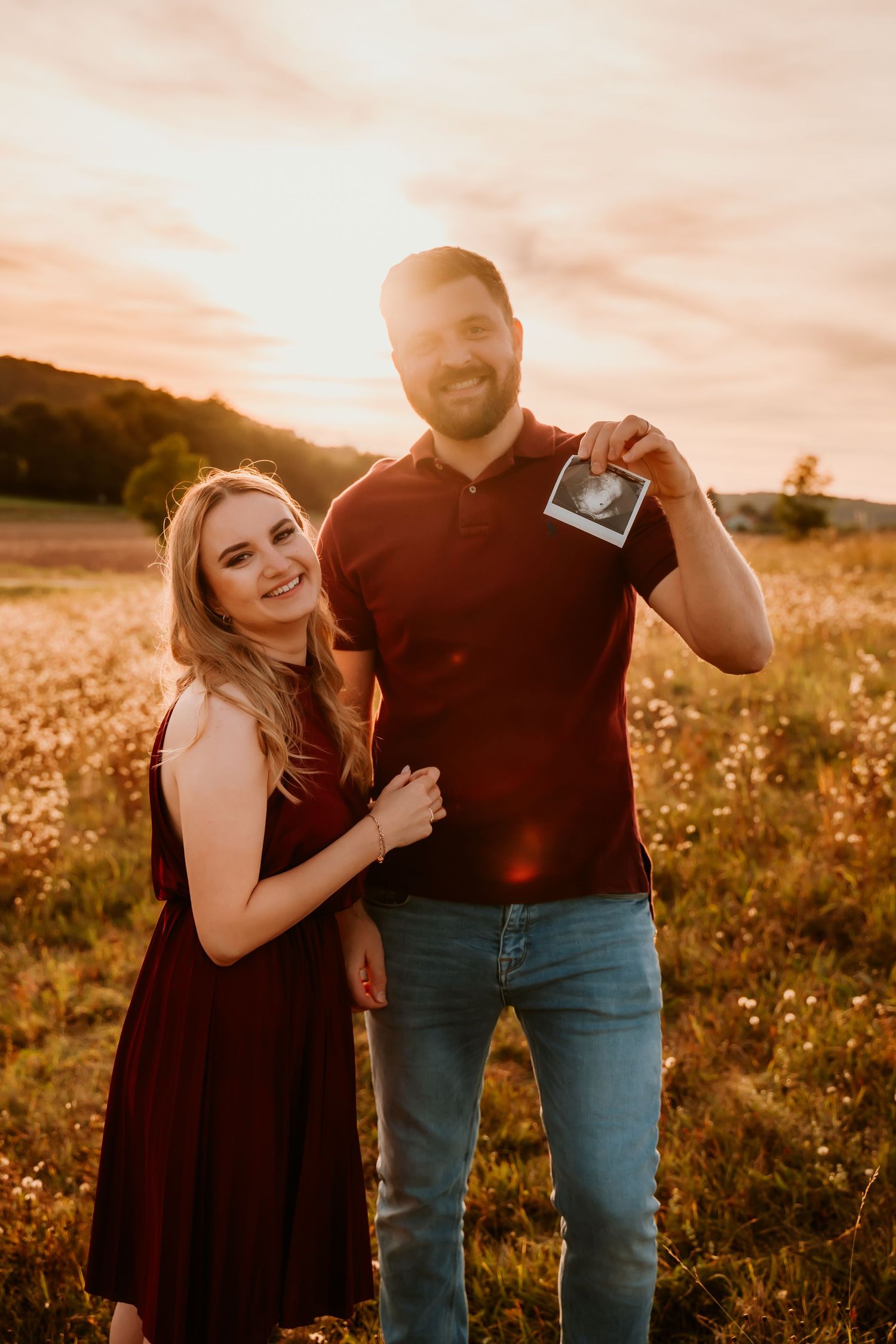 A couple shares a joyful moment while displaying a small photograph in a sunlit field.