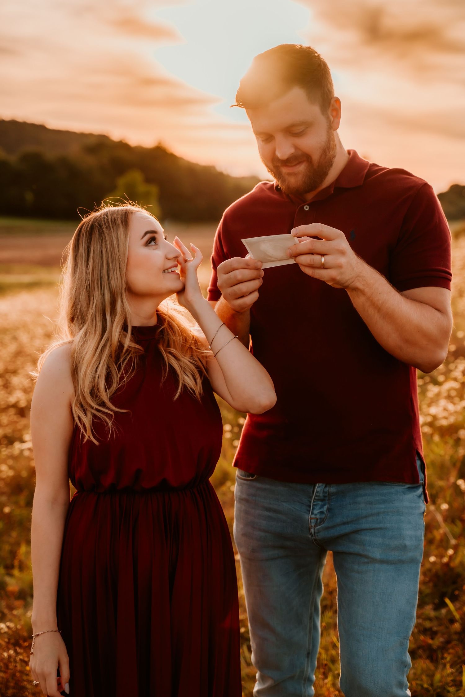Two people share a happy moment while looking at something in a sun-drenched field.