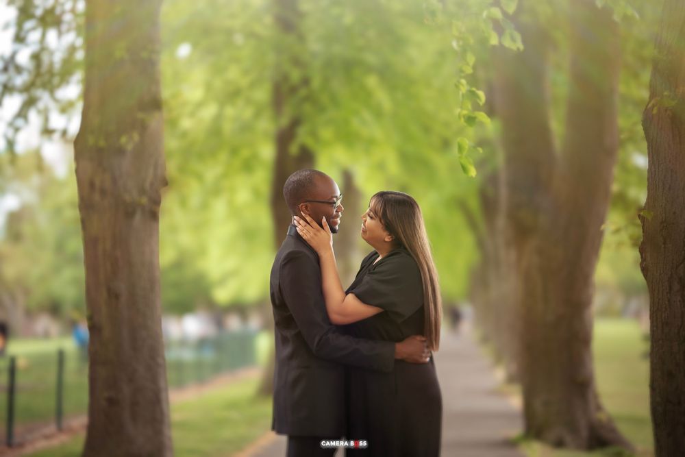 An intimate portrait of a couple embracing on a sunlit garden path surrounded by lush green trees.