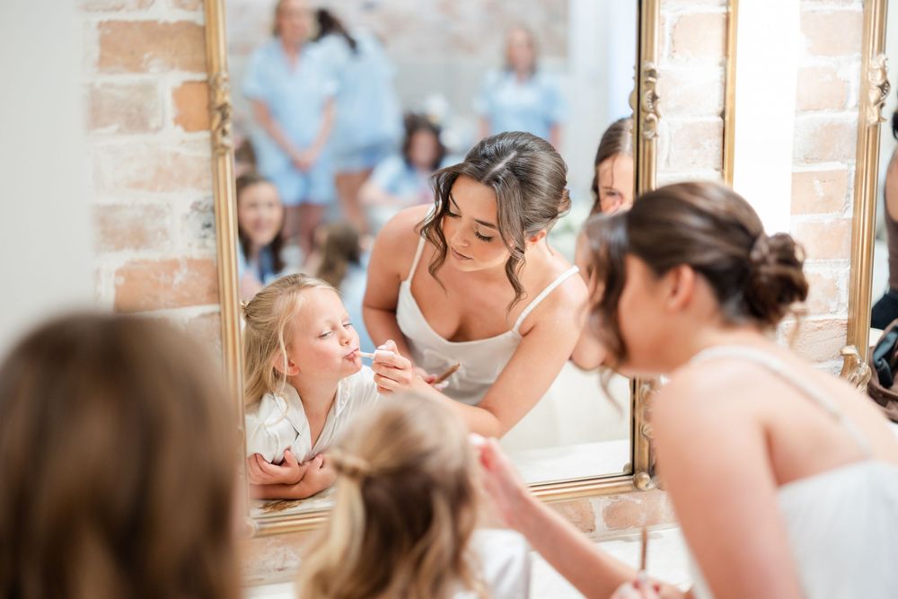 A candid moment of bridesmaids getting ready in a dressing room with exposed brick walls and mirrors.