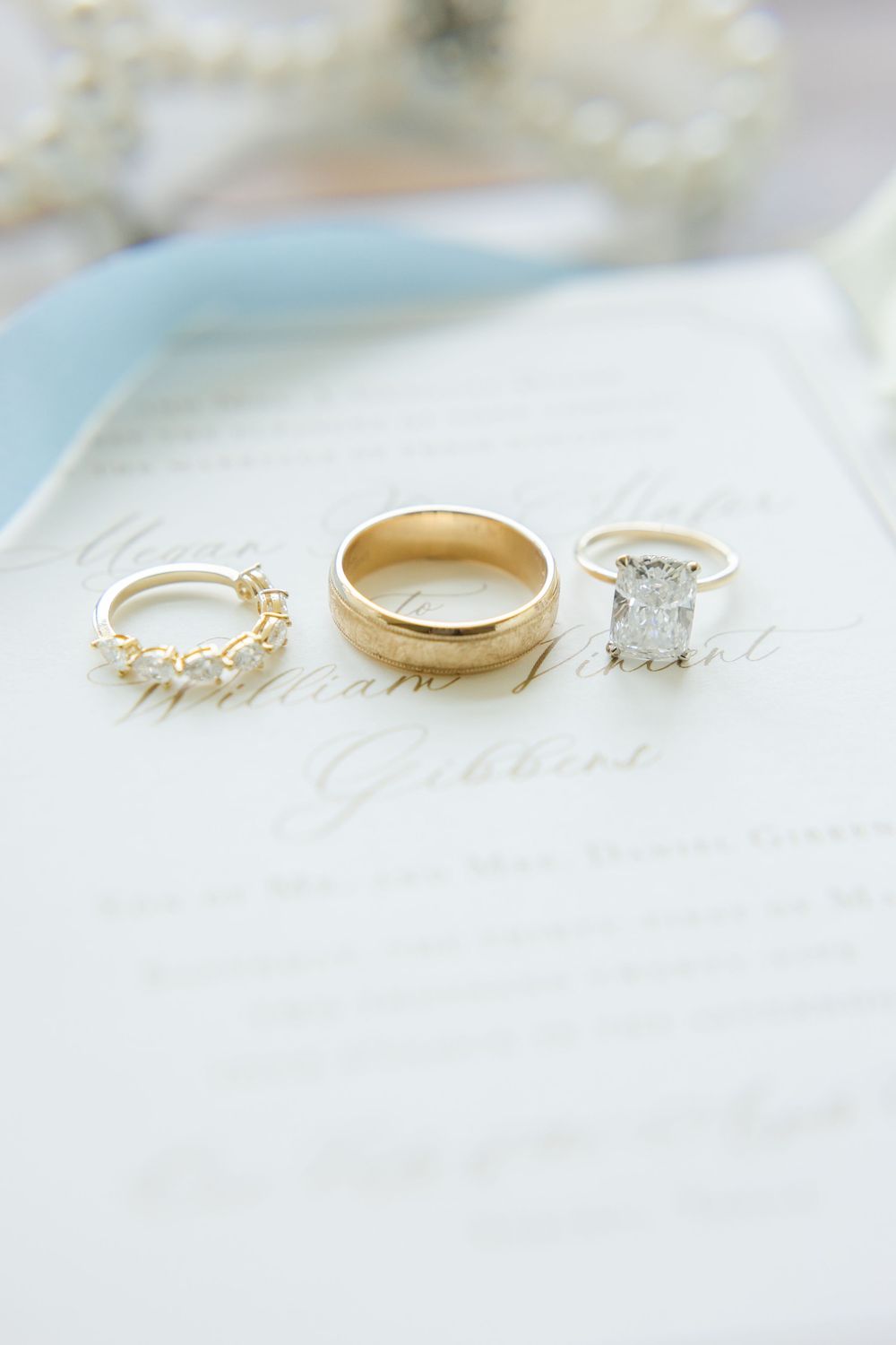 Three elegant wedding rings displayed on light blue and white fabric.