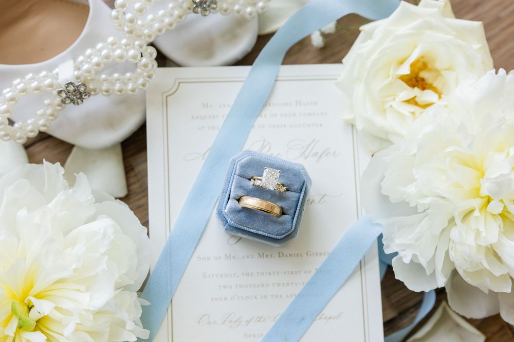 Wedding rings displayed in a blue velvet box with white peonies and ribbon on sheet music.