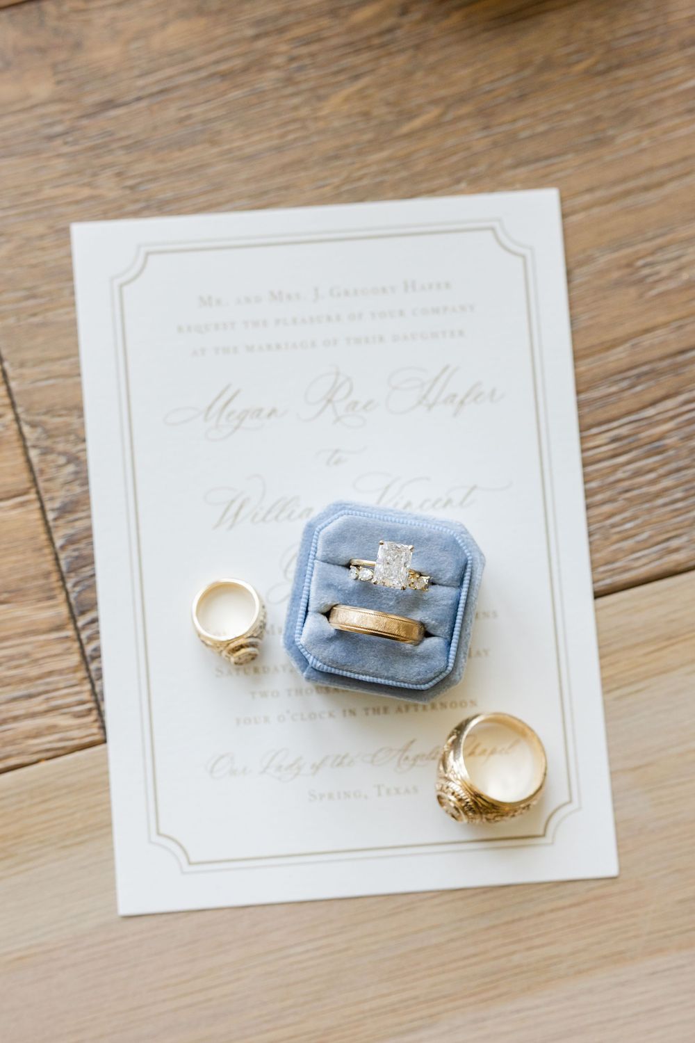 Wedding invitation with rings and blue velvet ring box on wooden surface.