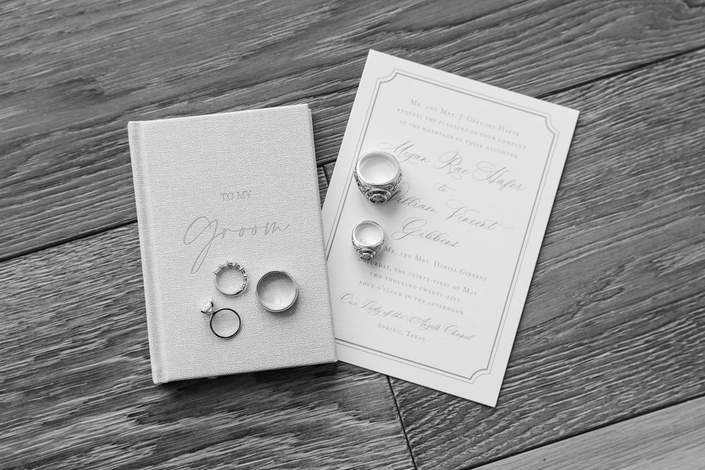Wedding rings and invitation suite arranged on gray wooden background.