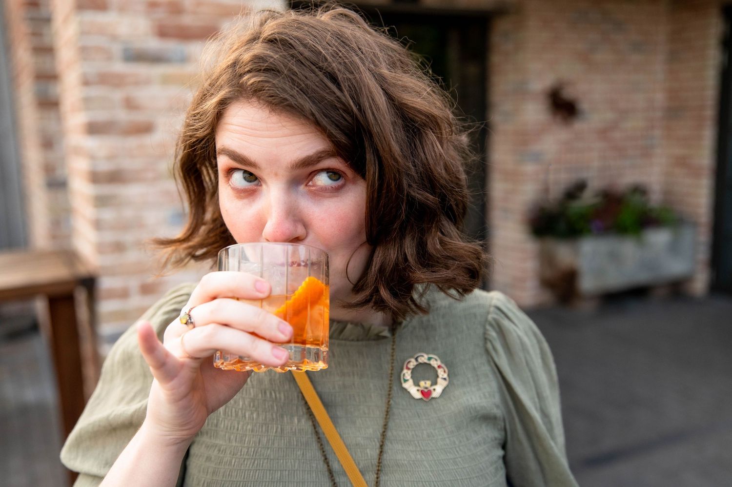 Someone takes a big bite of an orange ice cream popsicle while sitting outdoors.
