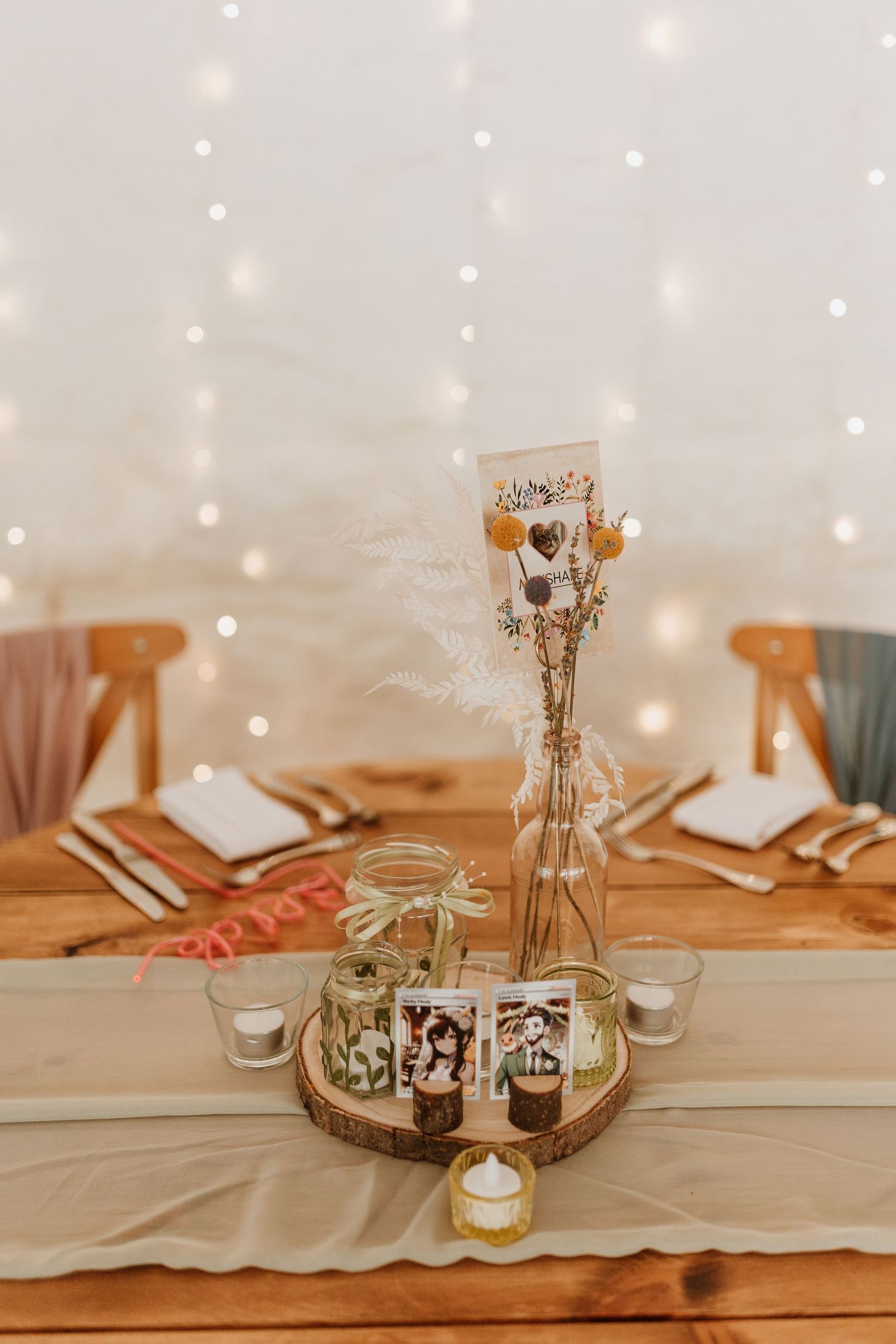 A rustic table setting with dried flowers in a vase, mason jars, and wooden decor illuminated by soft fairy lights.