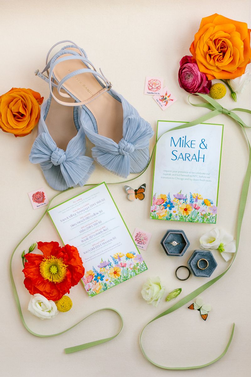 Elegant flat lay of bridal shoes, invitation, and rings with floral arrangements, captured by NYC wedding photographer Paula Brearley.