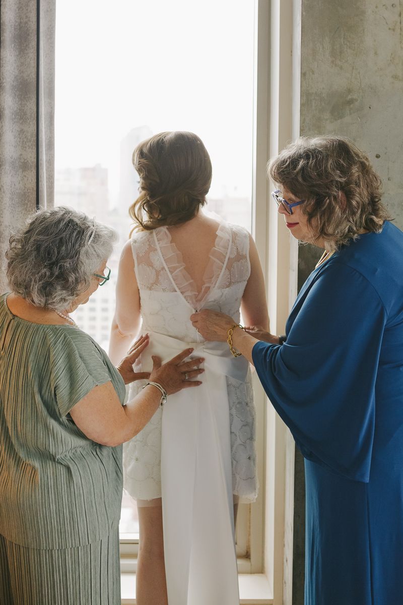 Mom and mother-in-law helping the bride get dressed, a heartfelt moment captured at her NYC wedding ceremony.