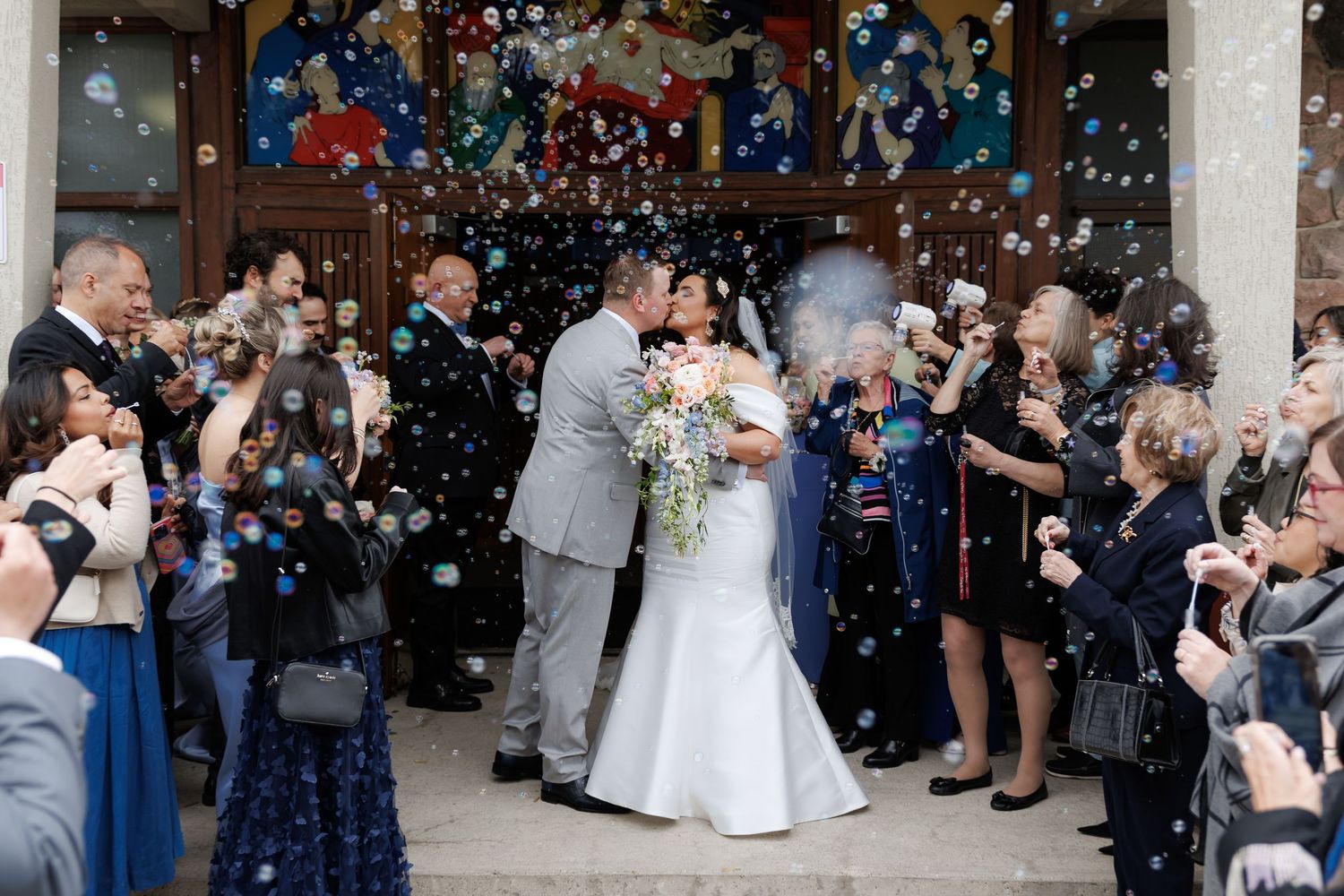 Wedding celebration with guests blowing bubbles as newlyweds exit the ceremony.