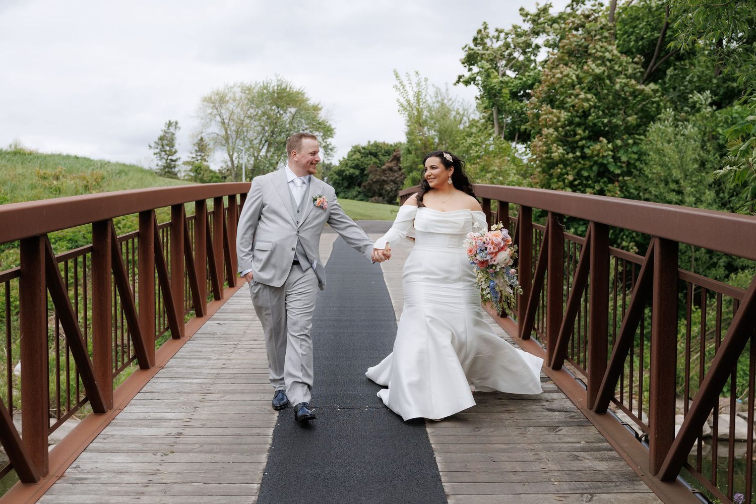 Newlyweds walking together on a wooden bridge in wedding attire.