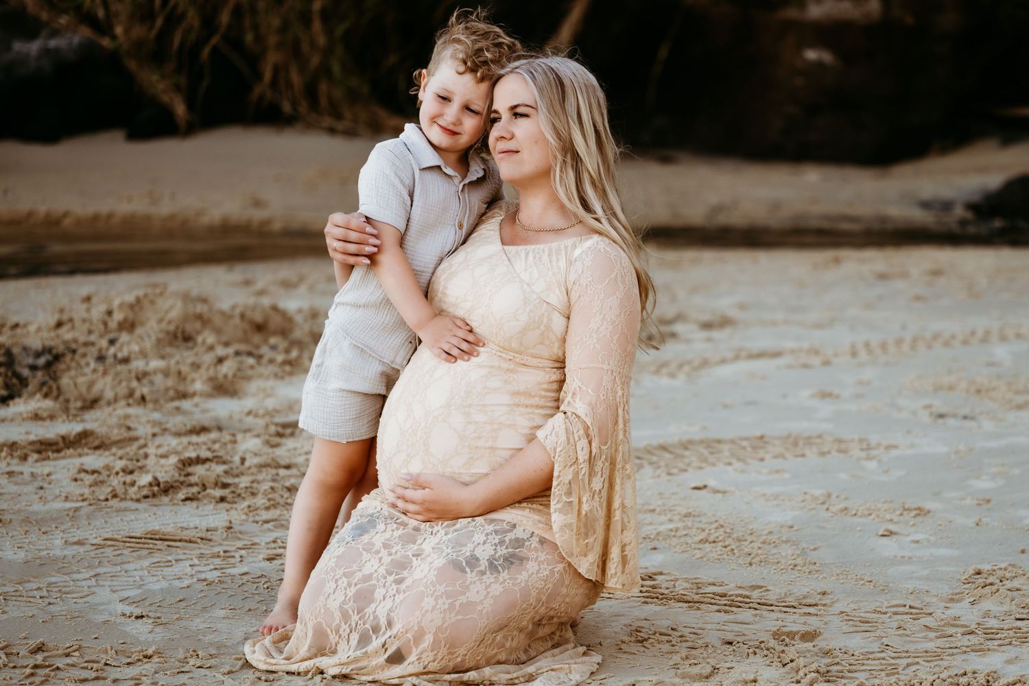 A tender beach maternity photo featuring a white lace dress and warm lighting at sunset on a sandy shore.