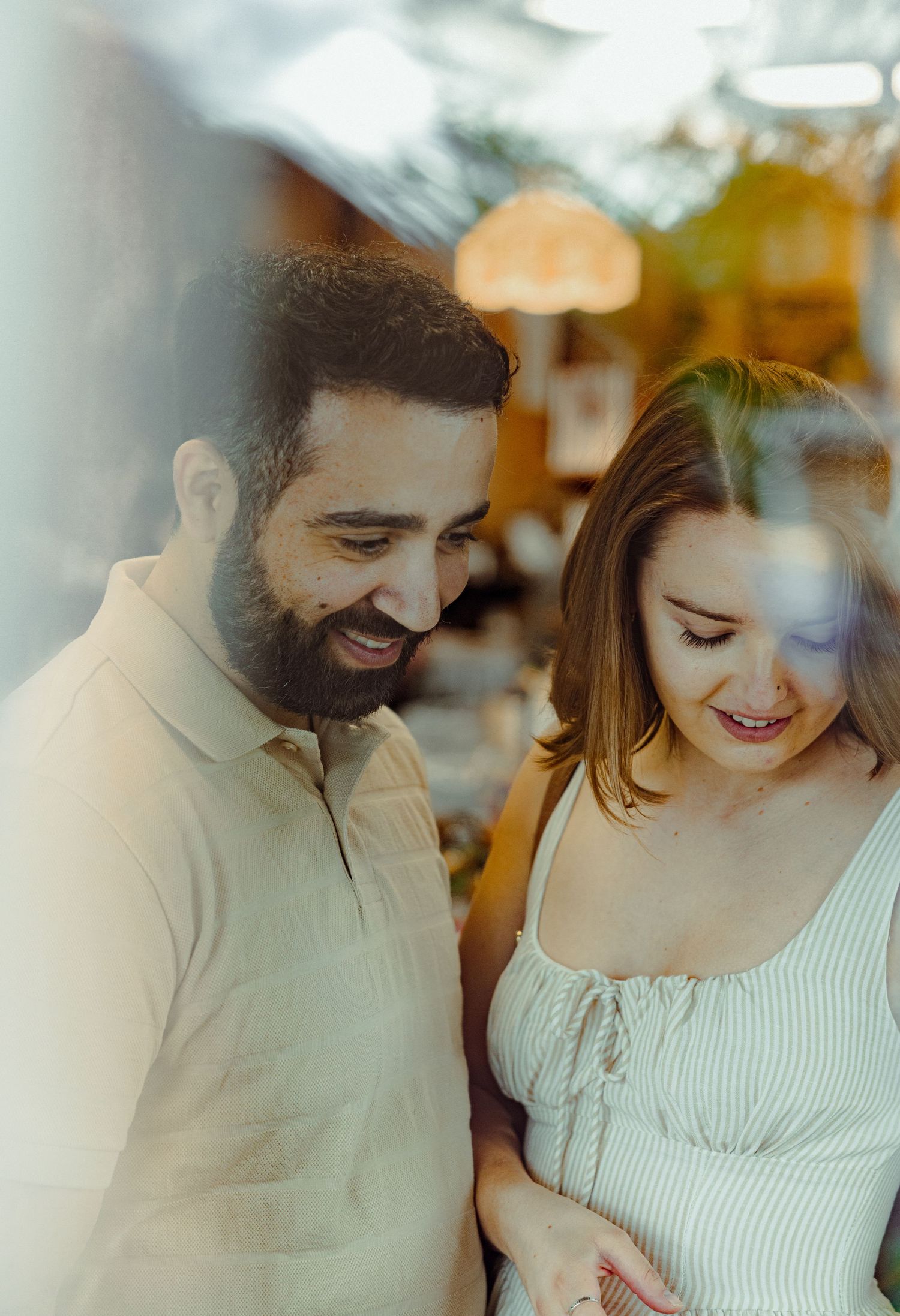 A happy couple share a tender moment together while smiling and looking down in warm indoor lighting.