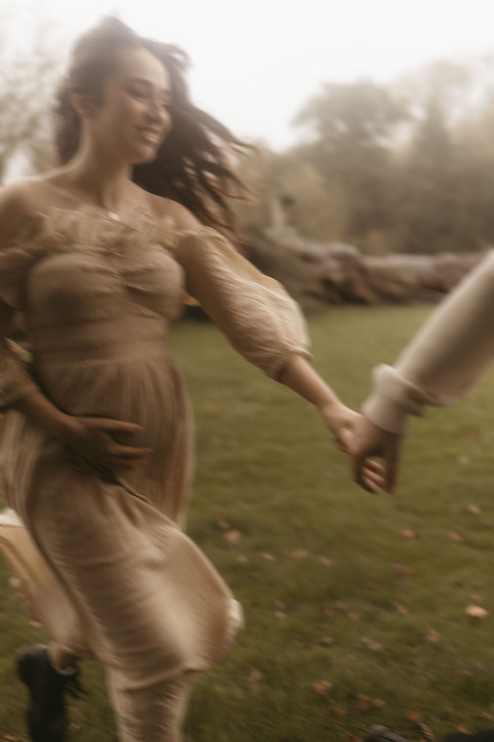 Motion-blurred figure in a brown dress spins playfully in a misty field at dusk.