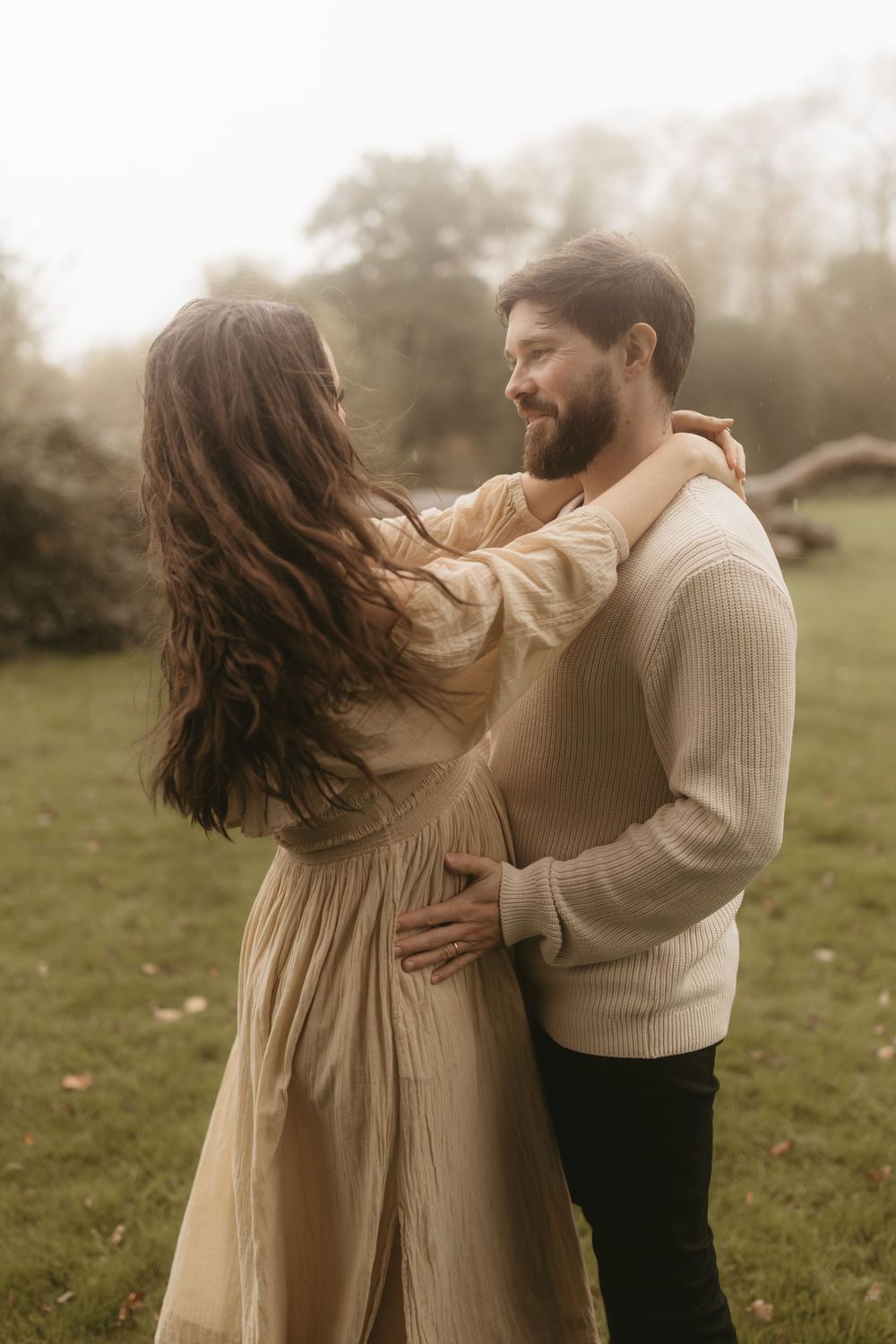 A romantic couple embraces in an outdoor setting wearing neutral tones and sharing an intimate moment in soft lighting.