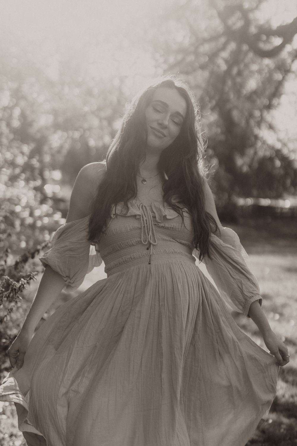 A flowing vintage-style dress twirls in an ethereal outdoor maternity portrait.