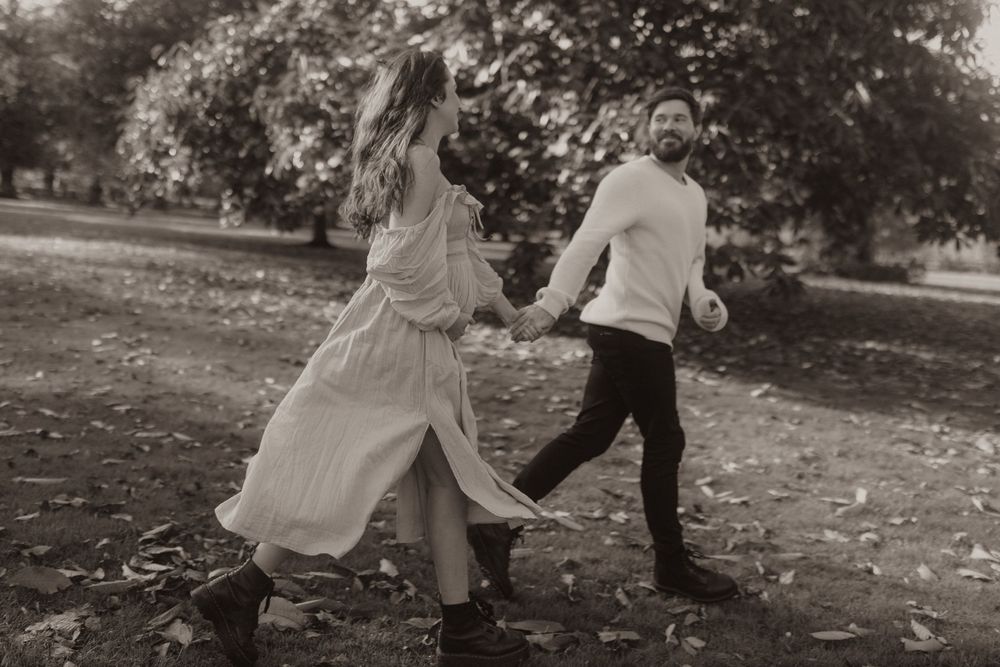 A vintage-style photo captures a couple dancing playfully in an autumn park setting.