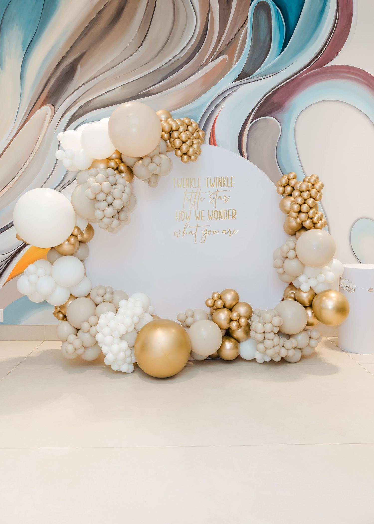 Elegant balloon arch installation with white and gold balloons against a flowing blue and beige backdrop for event decoration.