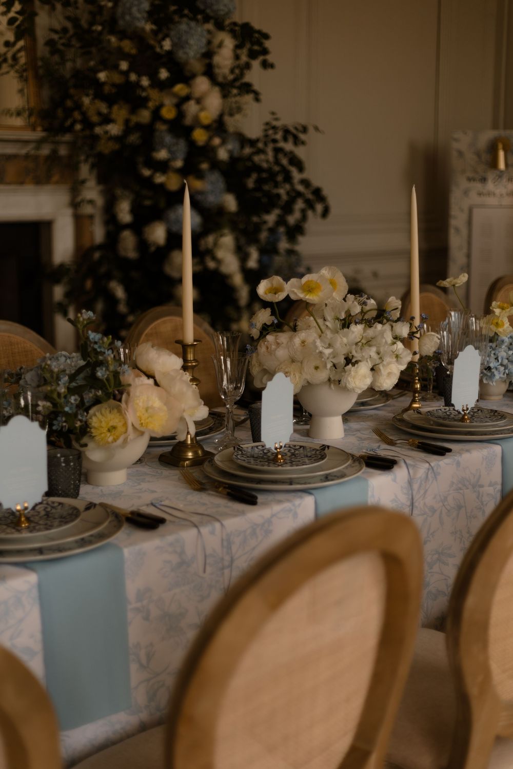 Elegant table setting with white floral centerpieces, tall candles, and vintage-style chairs at a formal dining event.