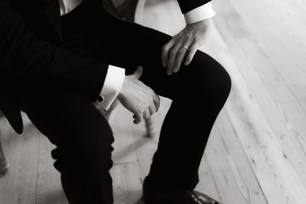 Black and white image showing hands folded while sitting on a wooden floor.