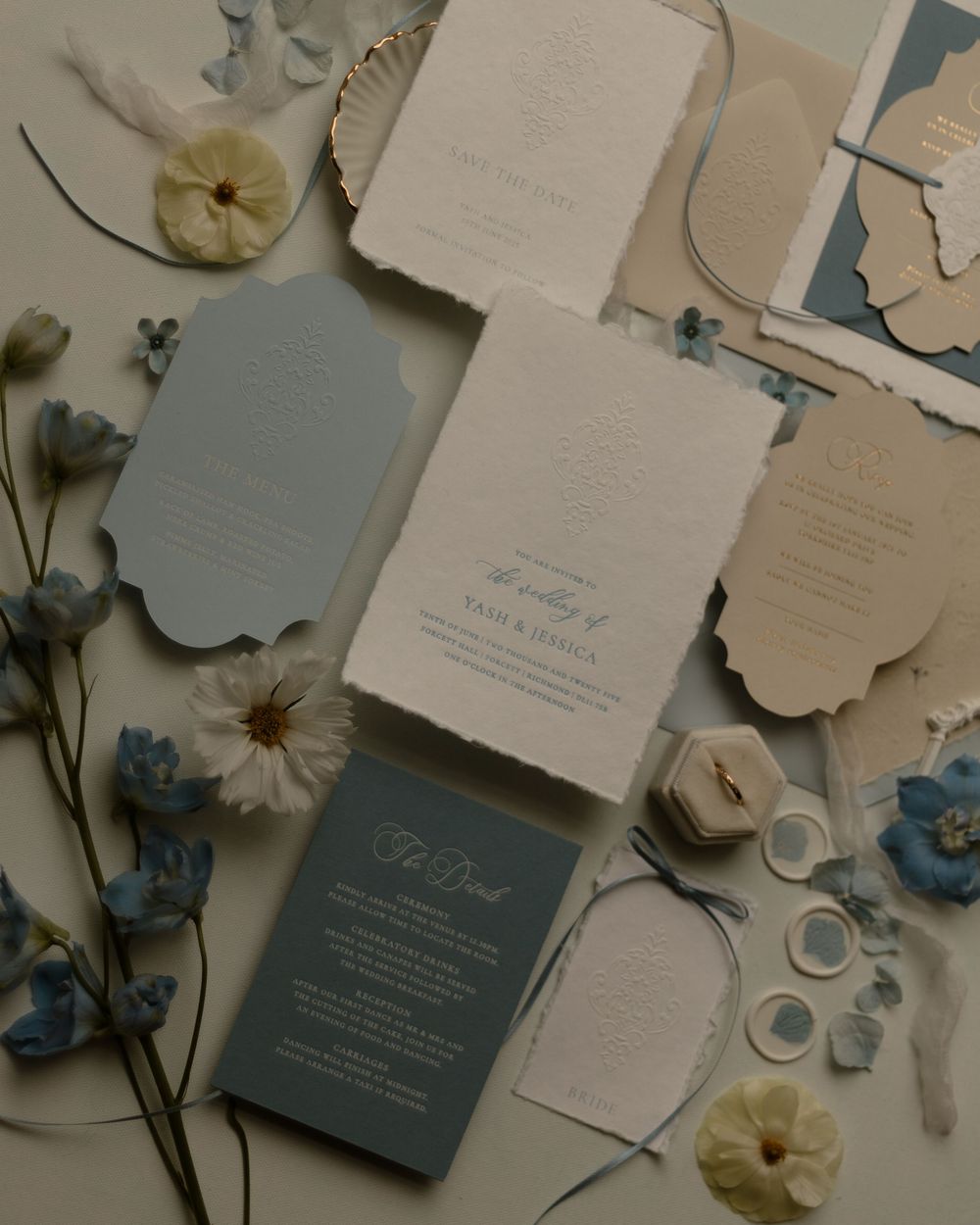 Wedding stationery featuring blue and white invitations with dried flowers and delicate details arranged on a neutral surface.