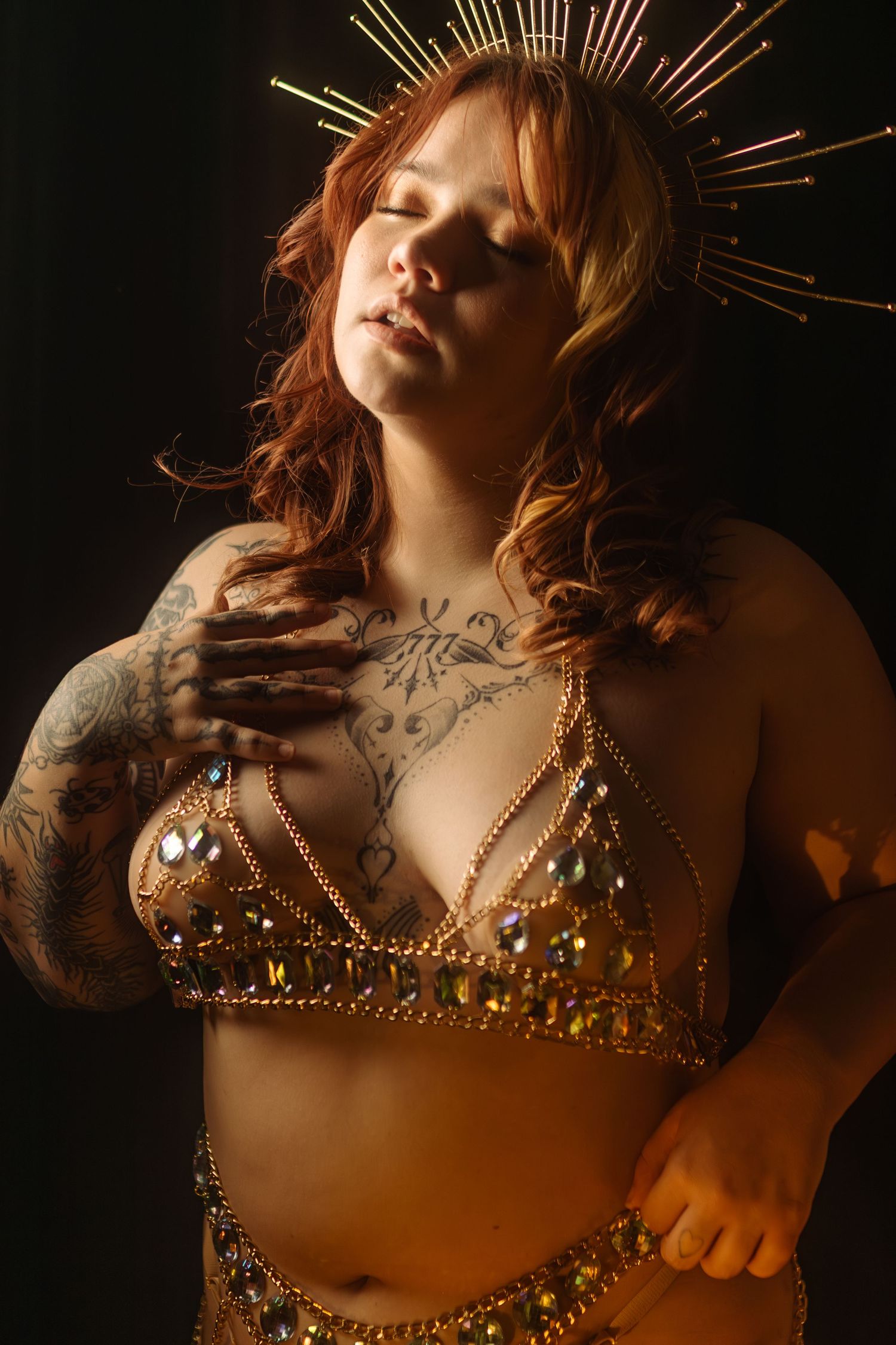 Artistic boudoir photo featuring a gold adorned bralette, crown-like headpiece, and delicate body art in dramatic lighting in Texas.