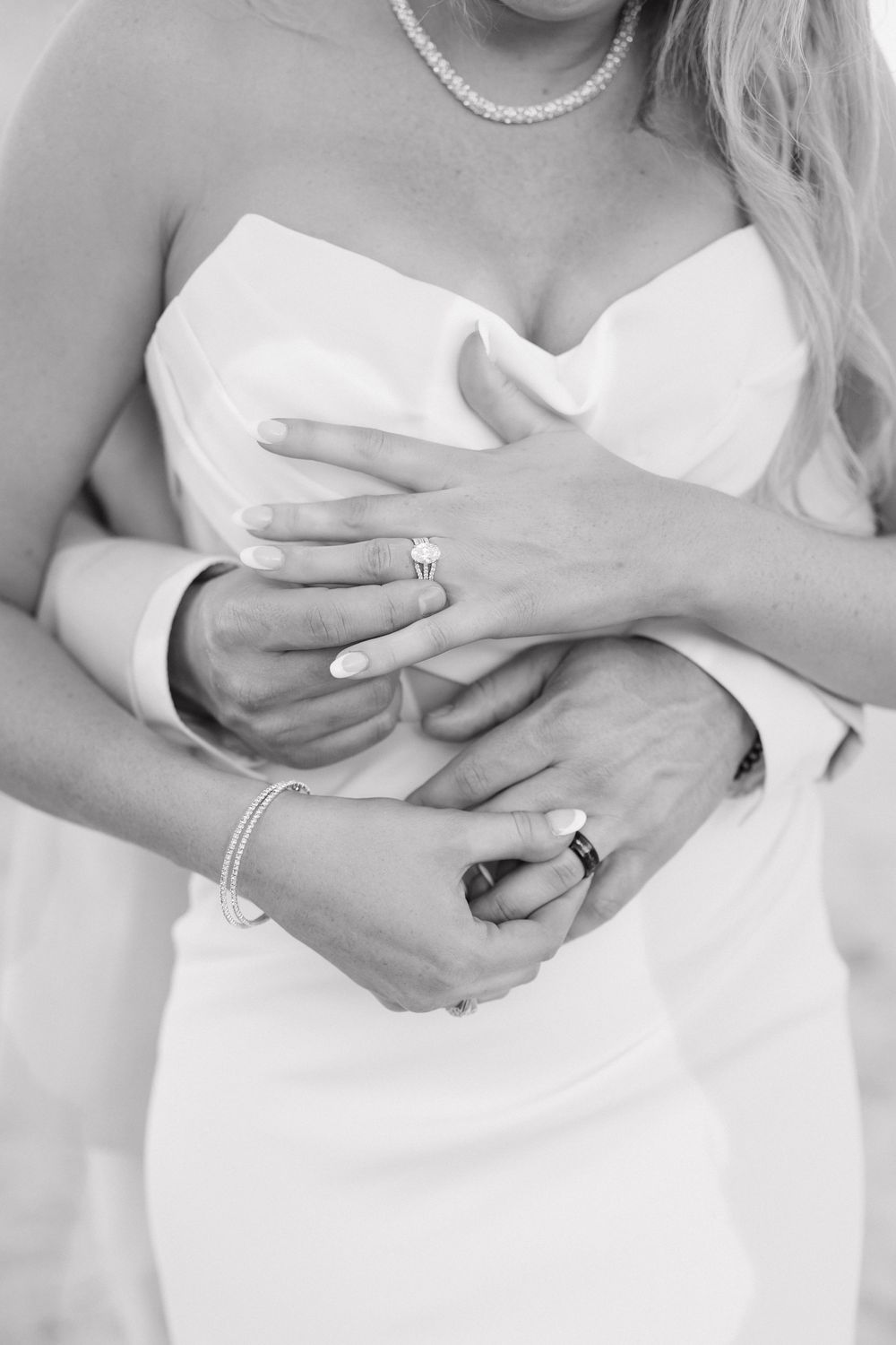 Black and white photo of hands embracing in a white wedding dress with pearl necklace and bracelet accessories.