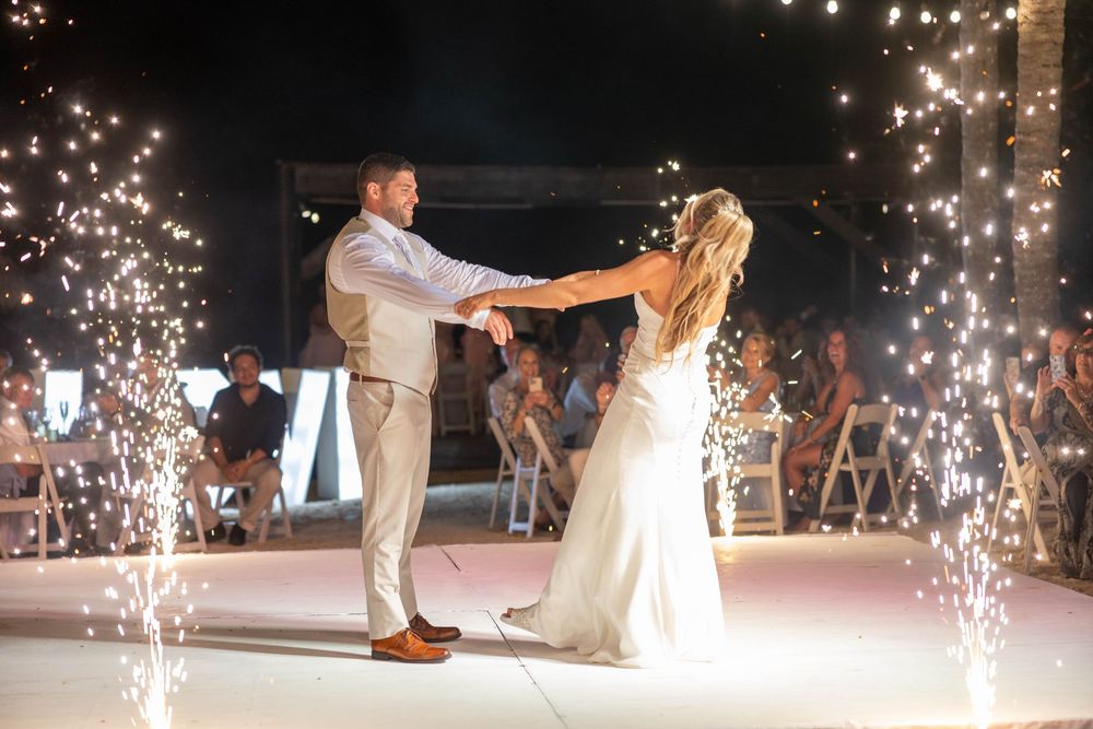 A couple shares their first dance on a white floor surrounded by sparklers creating a magical wedding moment.