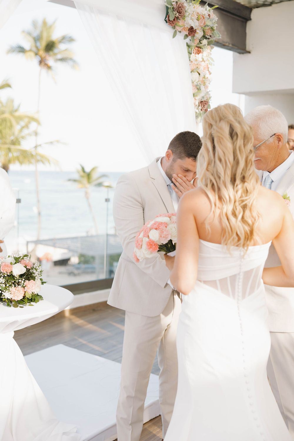 A romantic beach wedding ceremony with floral decorations and palm trees in the background.