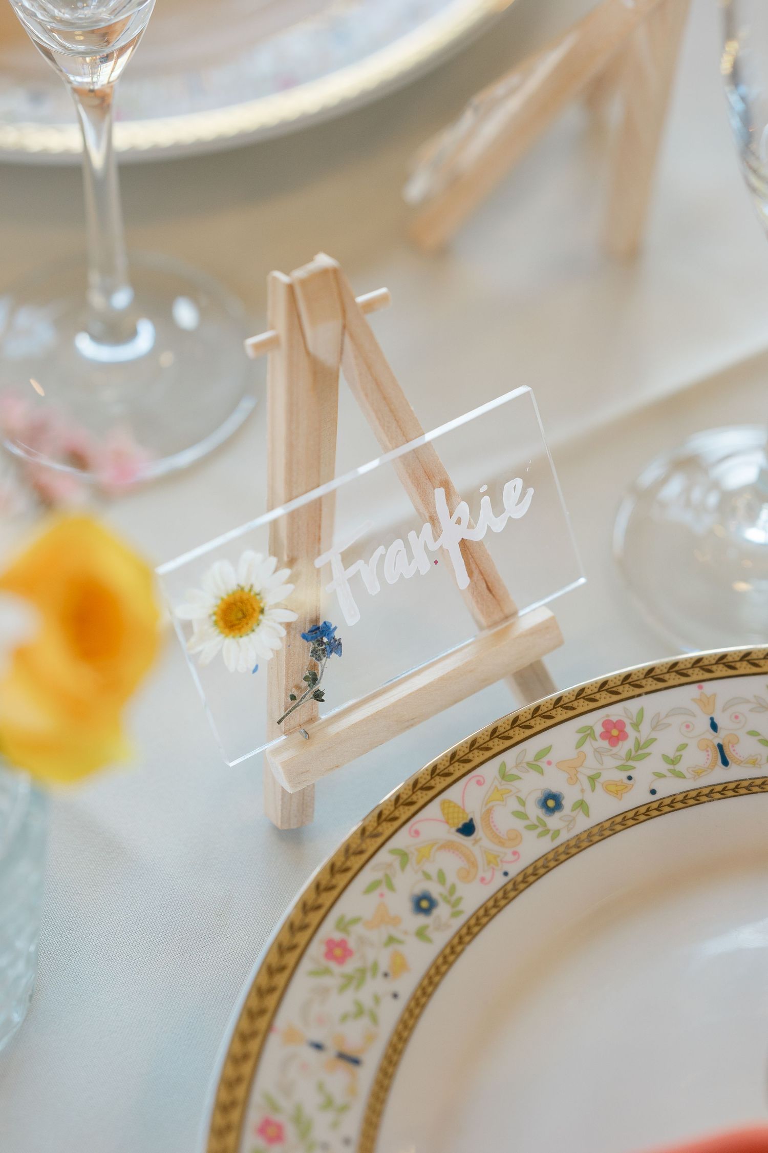 Small wooden easel place card holder with 'Larry' name tag and blue flower accent on elegant table setting.