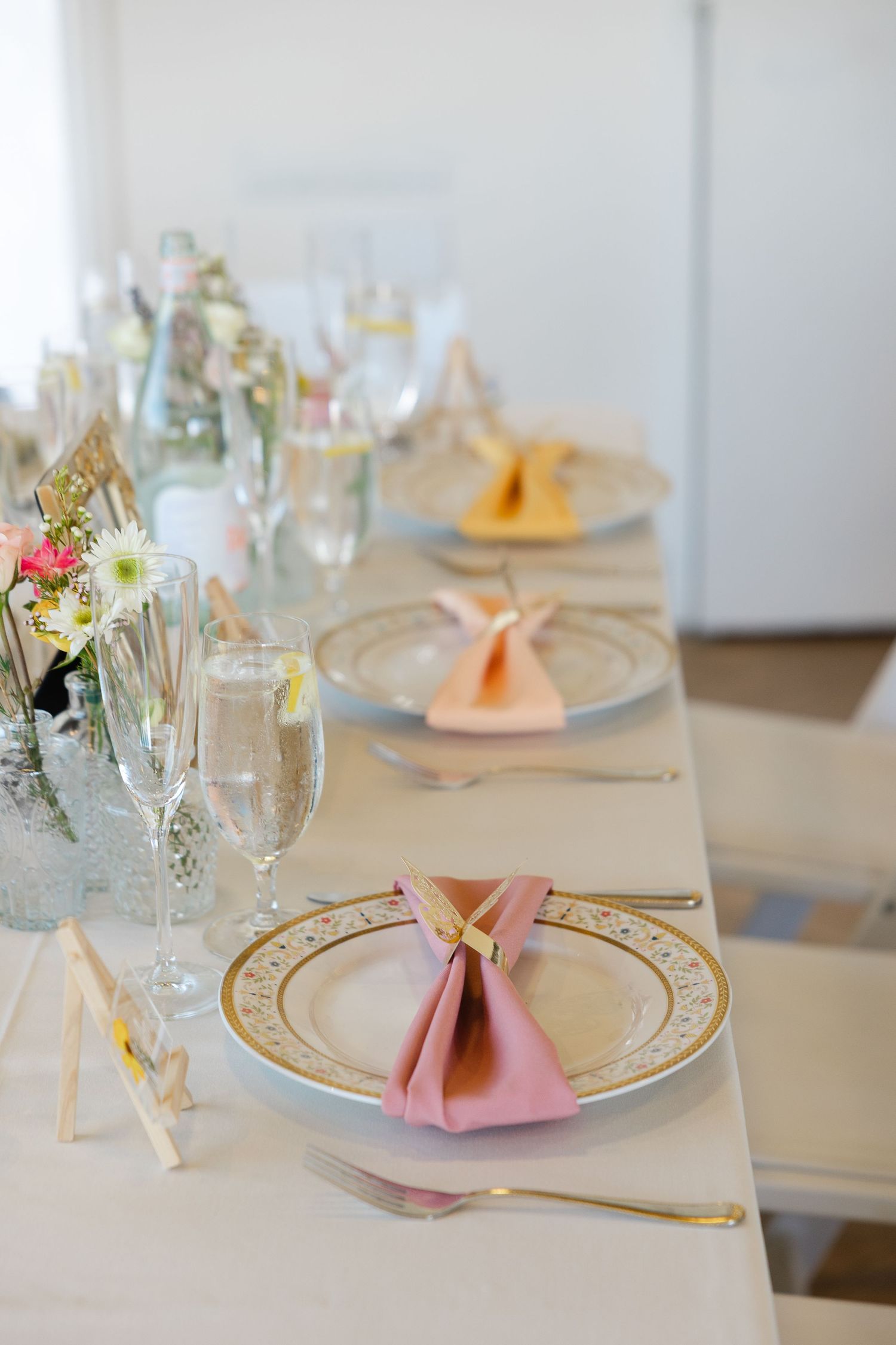 Elegant table setting with peach napkins, gold-rimmed plates, and delicate floral centerpieces for a formal event.