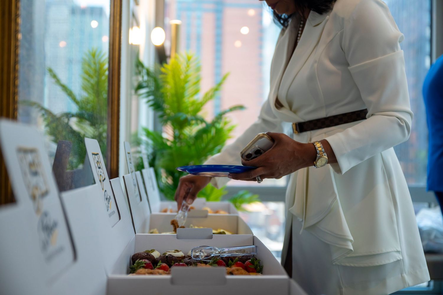 Professional in white blazer preparing catering service for event with food displayed on buffet table.