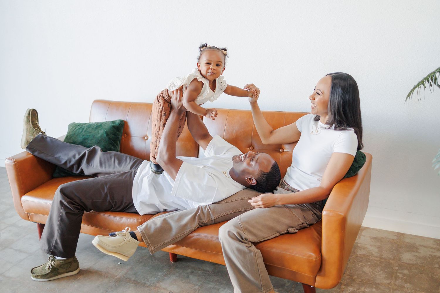 Happy family wearing neutral outfits relaxing on an orange couch in a Dallas studio during their family portrait session