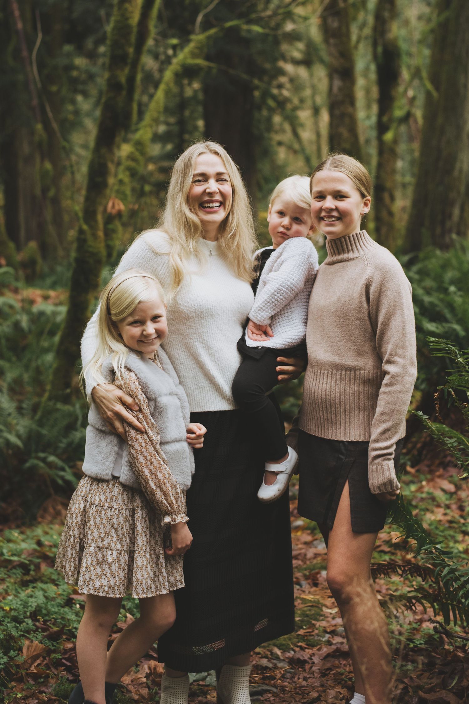 Mother smiles with her three daughters posing in the woods at goldstream provincial park.