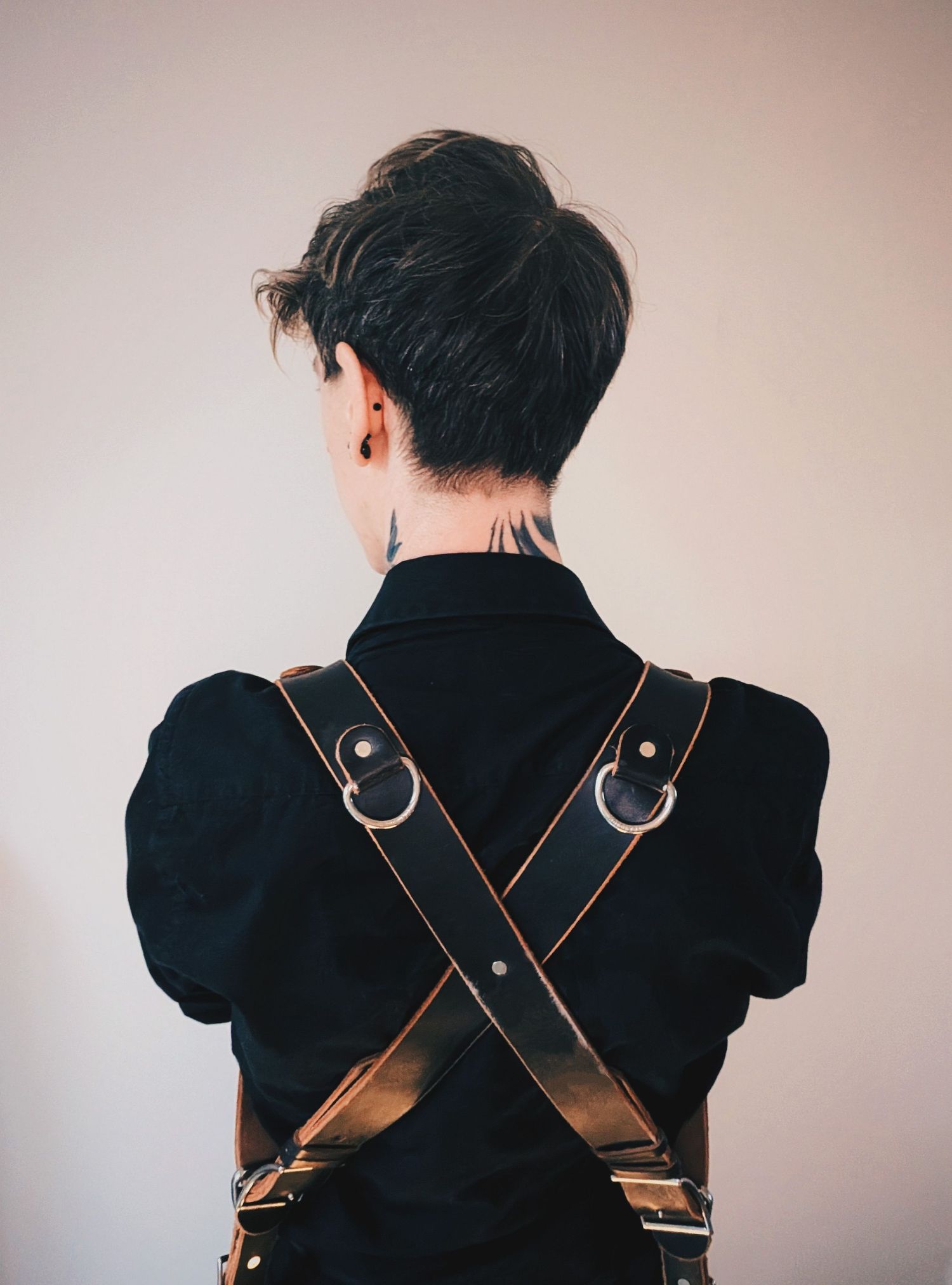 Back view of leather camera harness with crossing straps and metal hardware.