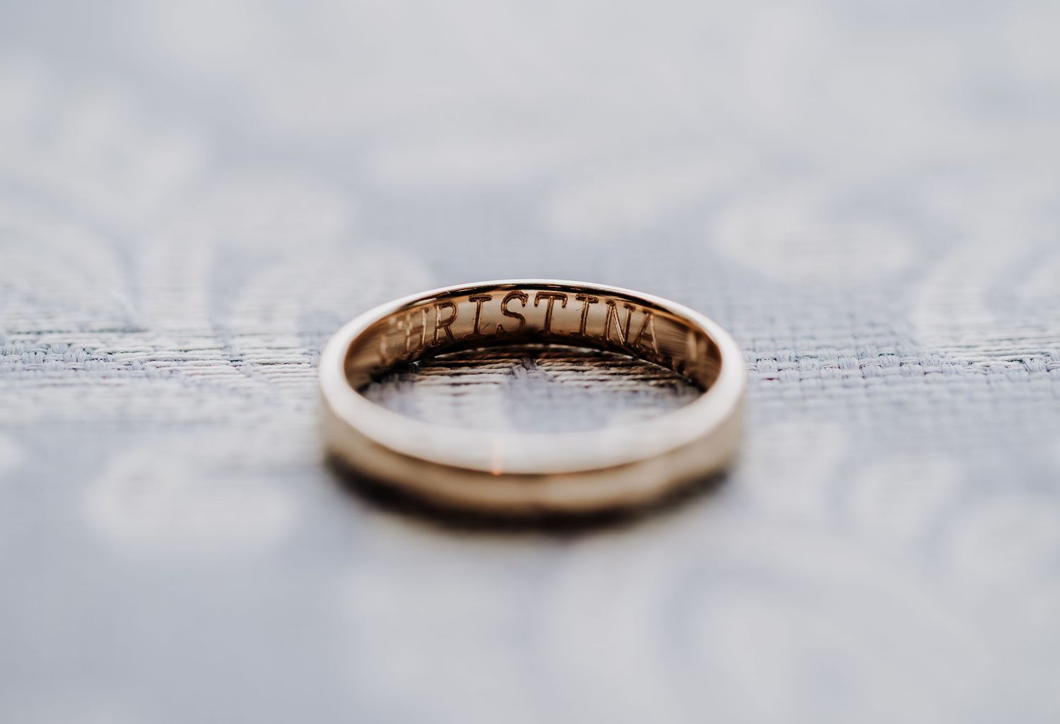 Gold wedding ring with engraved interior text photographed on a soft textured surface in macro detail.