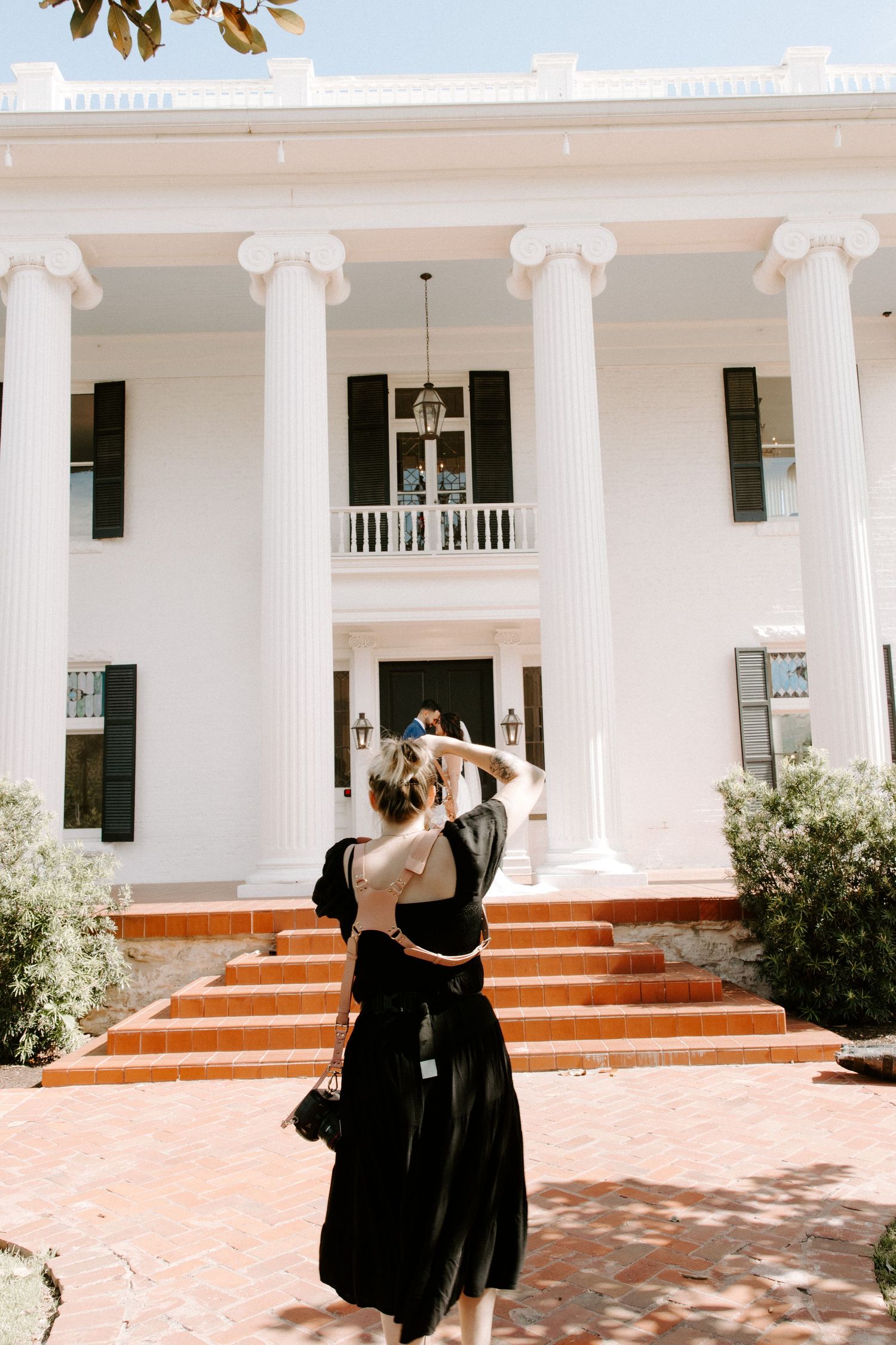 Person in black dress helping with bridal preparations outside a grand white columned building.