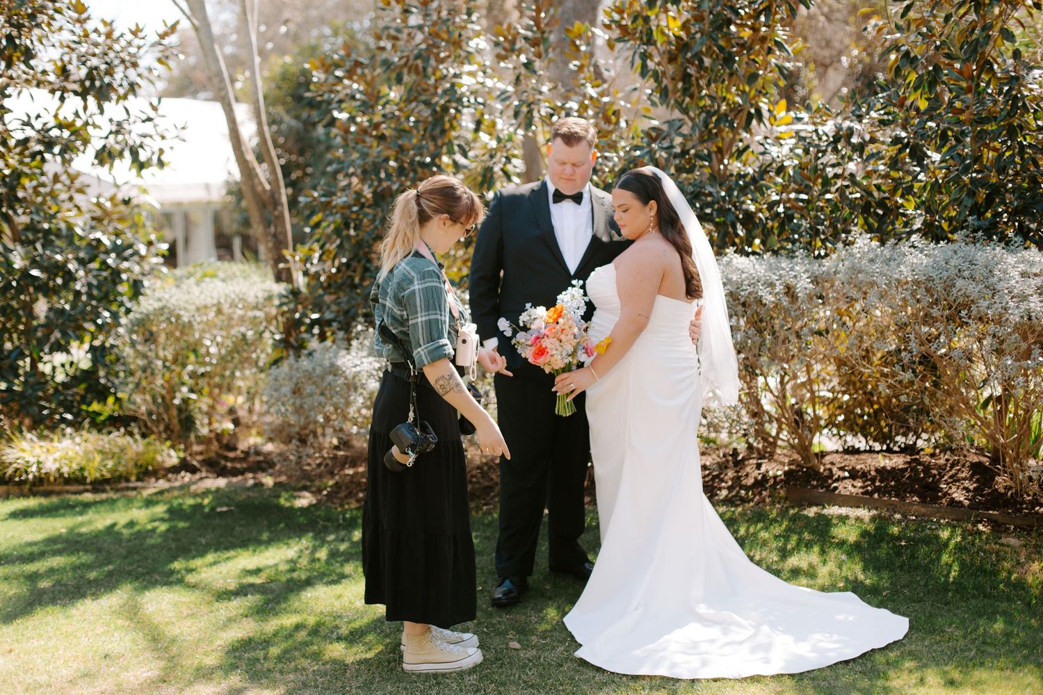 Wedding ceremony held outdoors with bride in white dress and officiant in black under autumn trees.