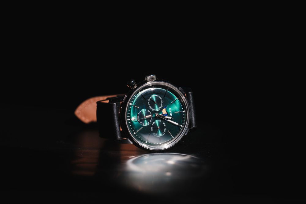 Modern wristwatch with glowing turquoise dial features displayed dramatically against black background.