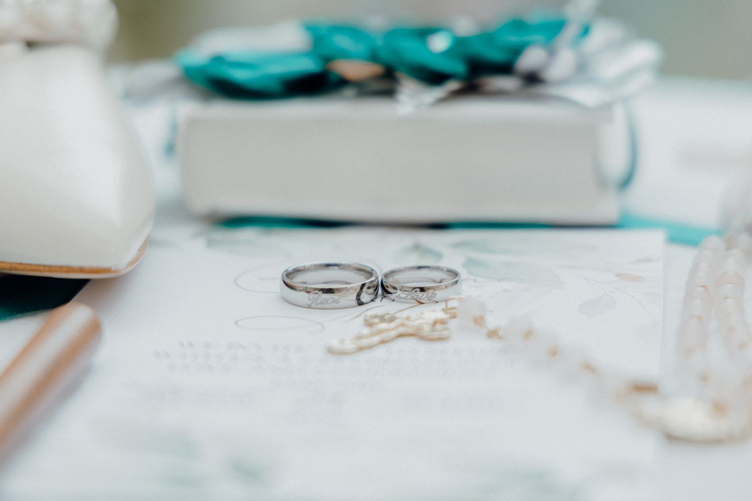 Two wedding rings resting on a white surface with a teal gift box in the background.