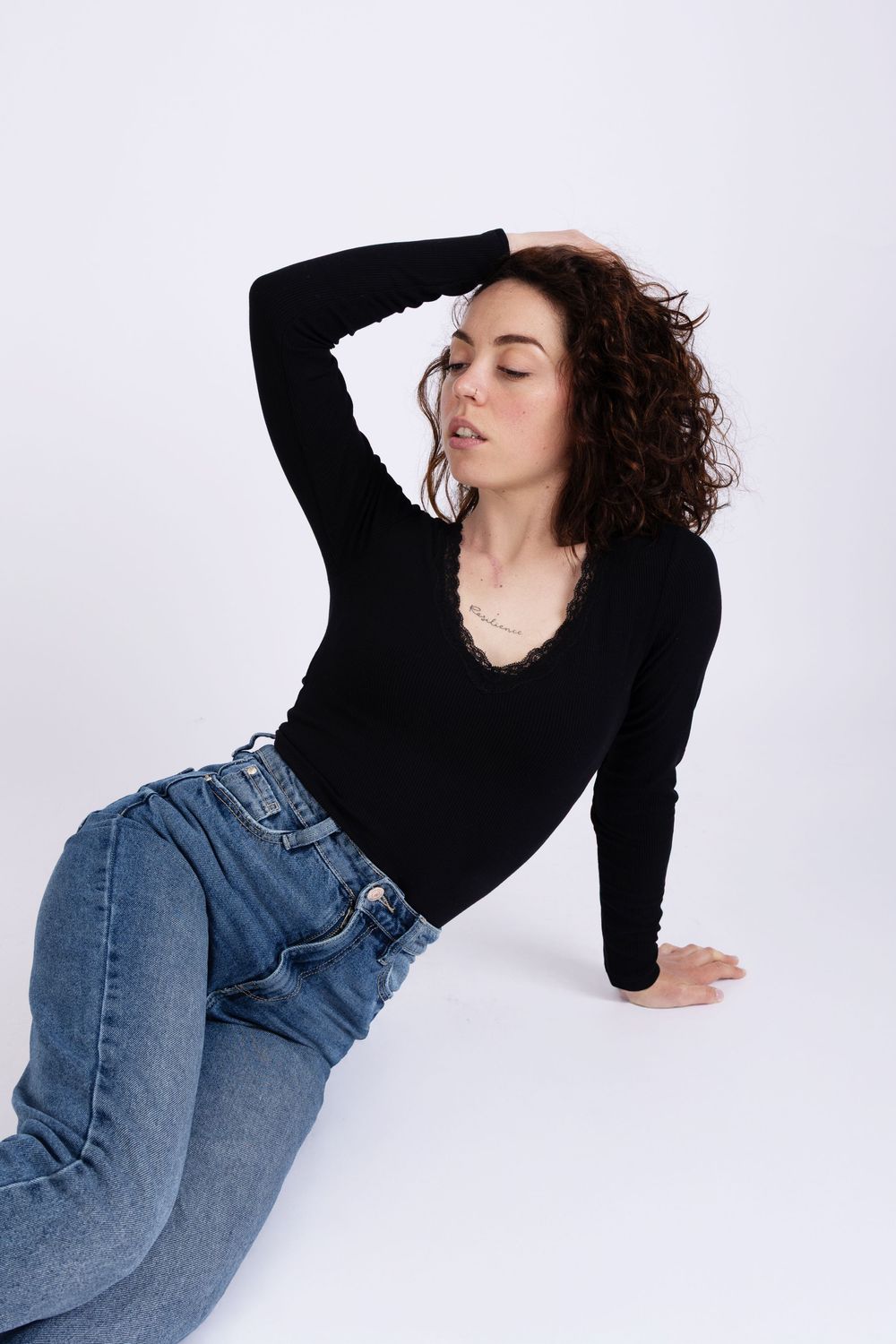A model in a black long sleeve top and blue jeans poses gracefully against a light gray background.