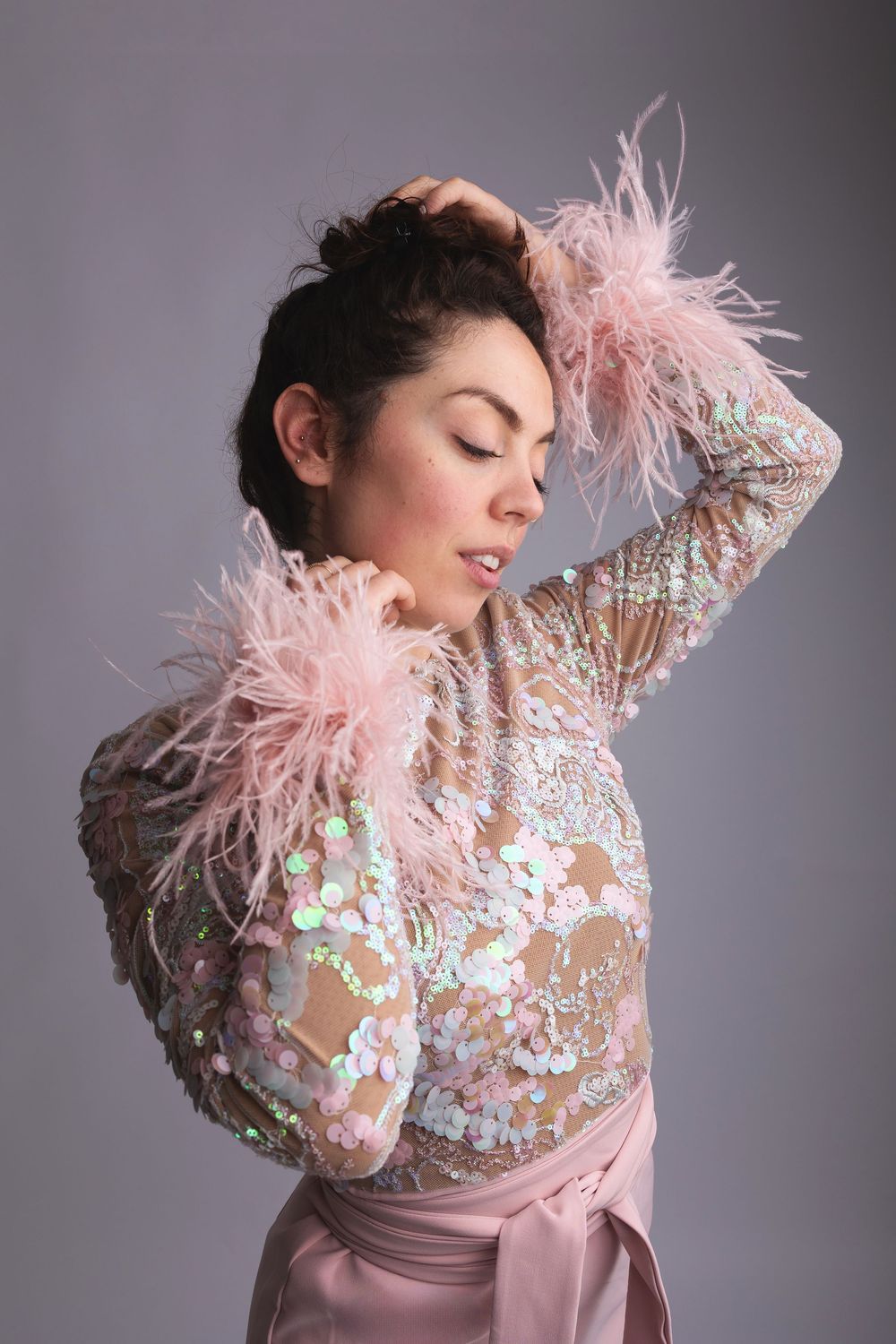 Fashion portrait of a model in a pink embellished sheer top with ostrich feather details and satin skirt.