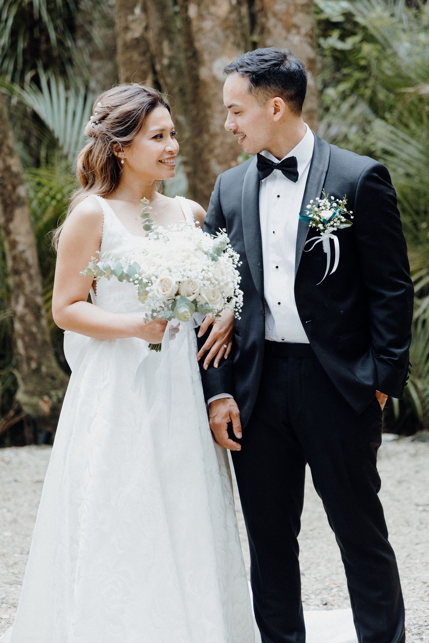A couple in formal wedding attire share a loving moment outdoors captured by Apertured Media Auckland Wedding Photographer.