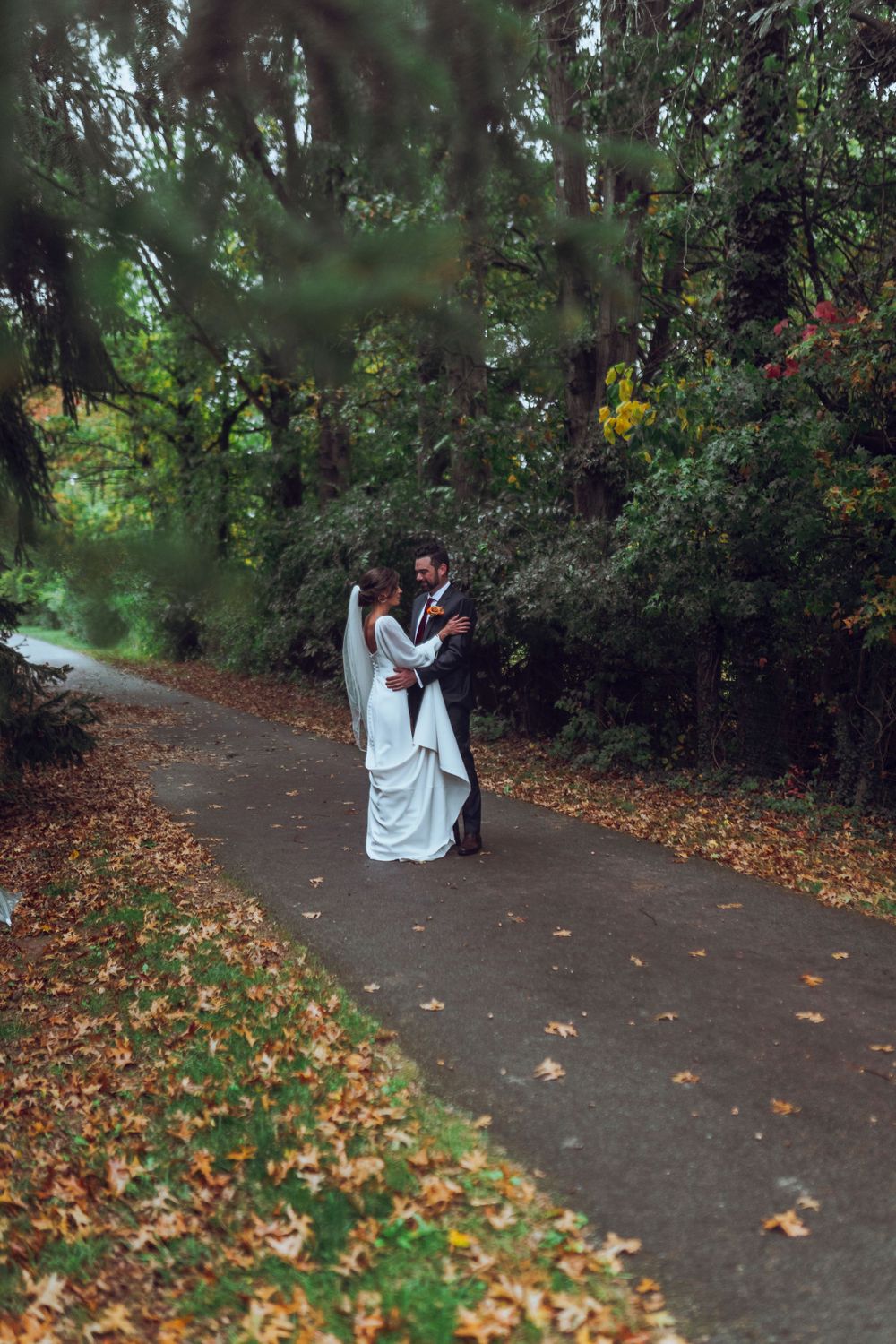 A bride and groom hold each other in the rain, smiling under clear umbrellas, capturing a romantic and joyful wedding moment.