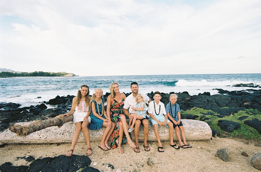 Group of friends sitting on rocky coastline with ocean waves in background.