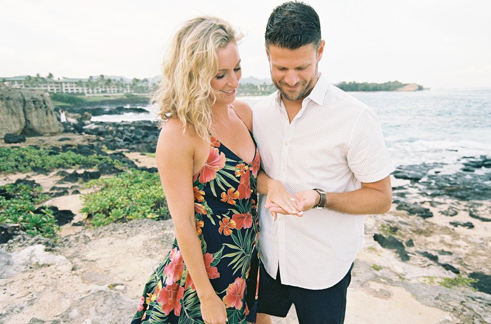 Couple in casual beachwear posing together on rocky Hawaiian coastline.