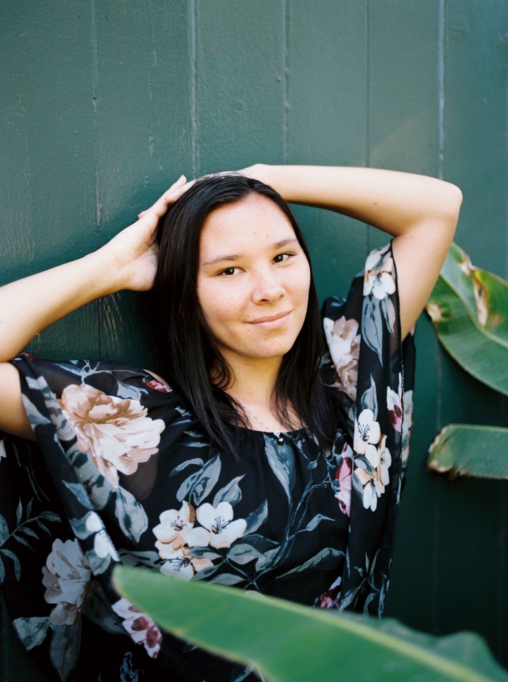 Portrait against green wall wearing floral top.
