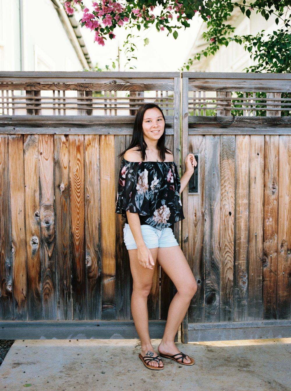 Summer portrait against wooden fence with pink bougainvillea flowers.